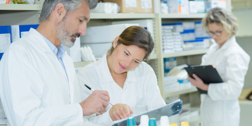 Three healthcare workers in white coats looking at clipboards