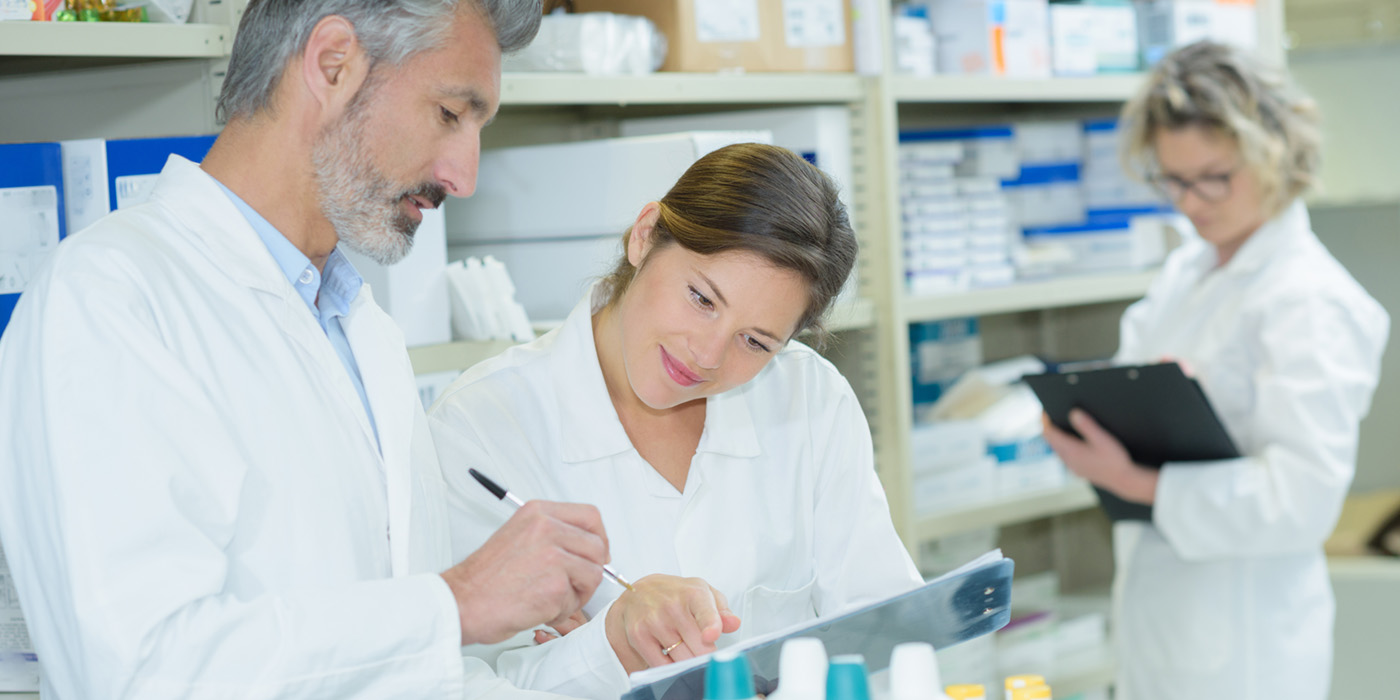 Three healthcare workers in white coats looking at clipboards